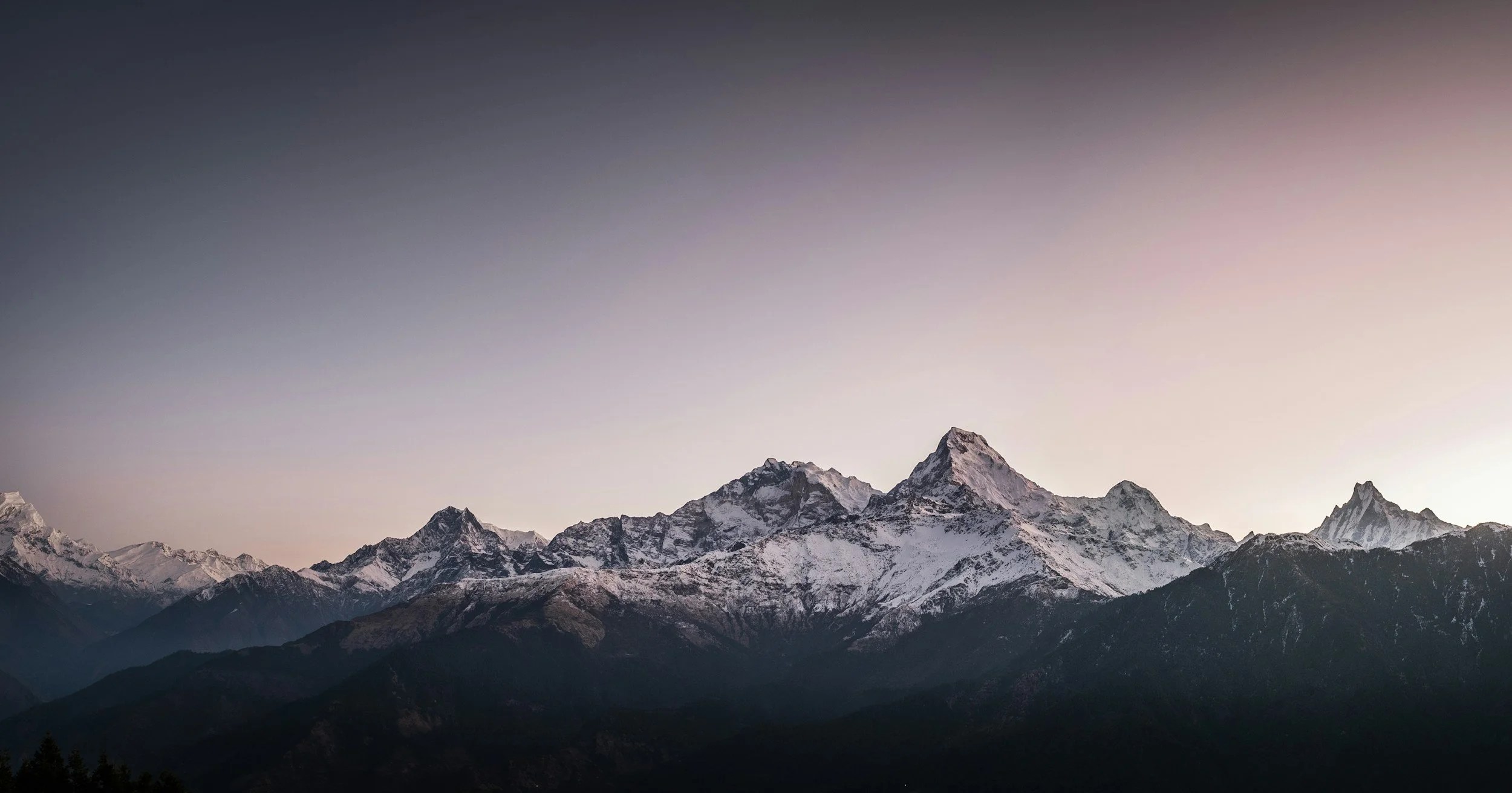 Snow-covered mountain range at sunrise with a clear sky.